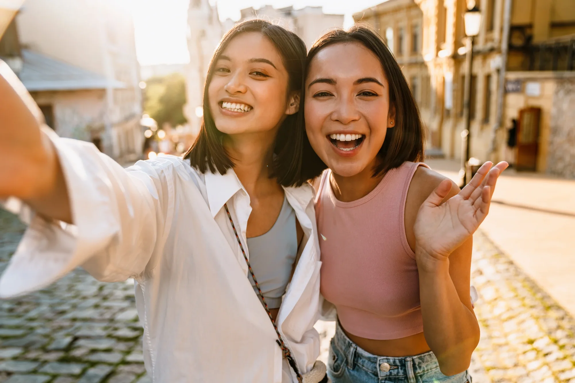 Two smiling friends taking a bright outdoor selfie.