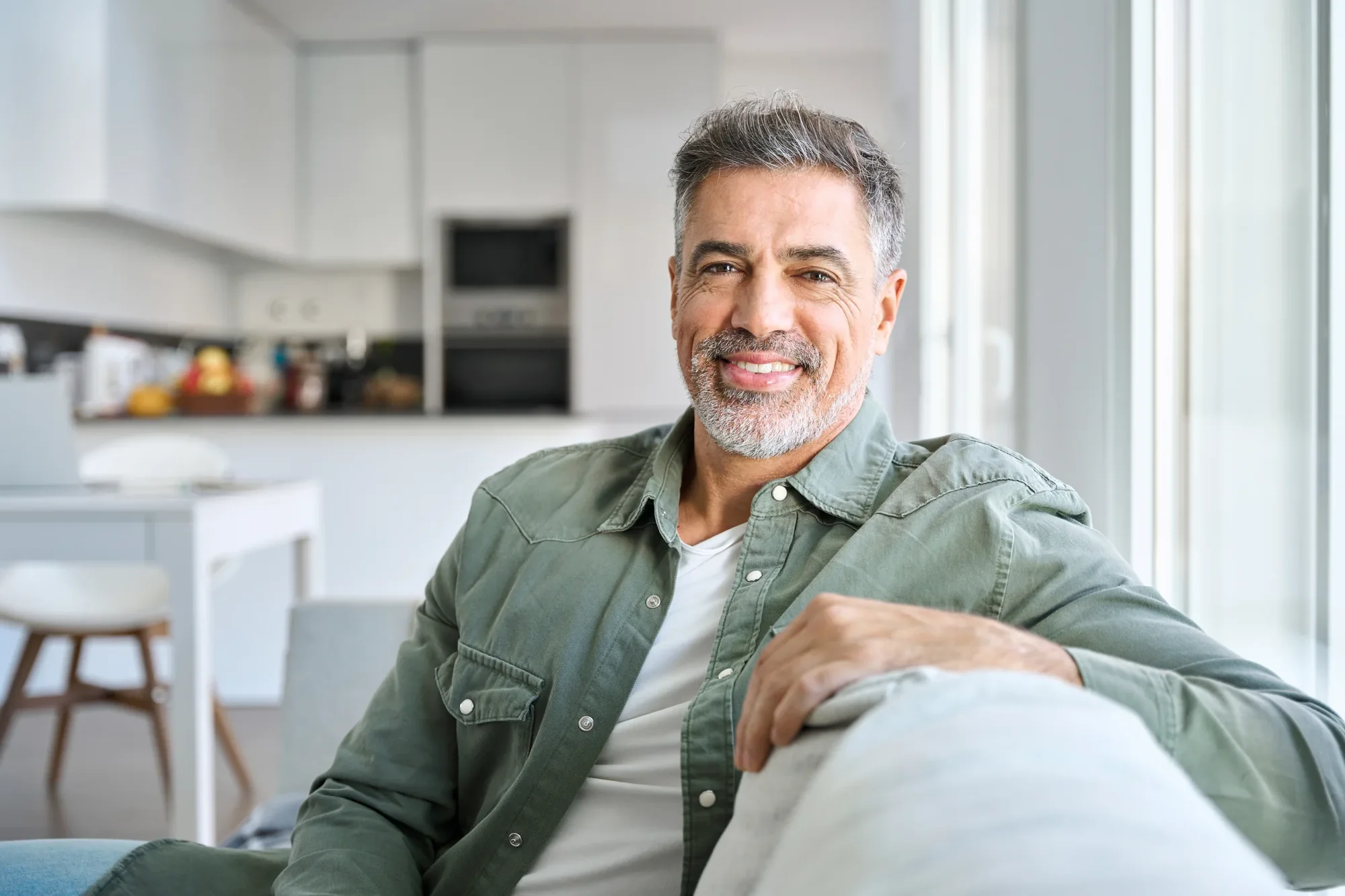 A smiling man seated in a bright home setting.