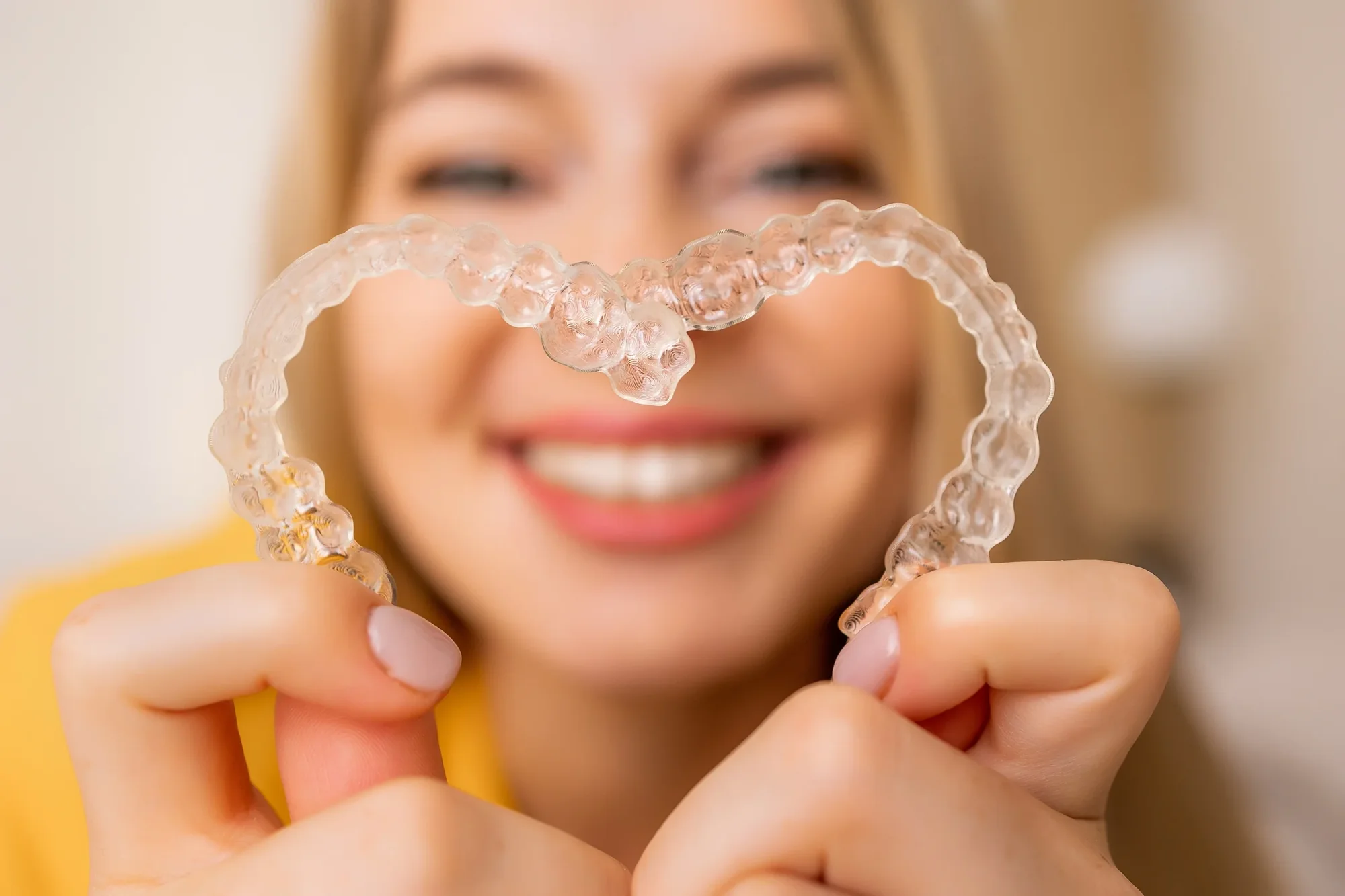 A smiling patient holding clear aligners.